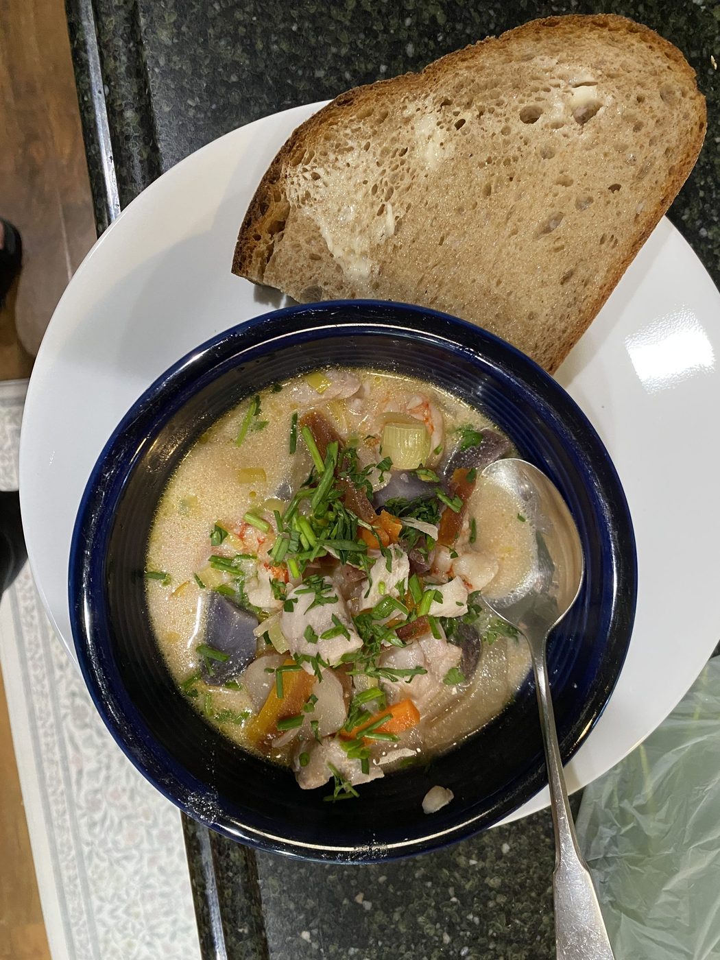 A blue bowl of creamy fish soup with herbs, and a thick slice of bread alongside