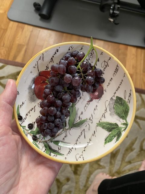 A hand holding a hand-painted plate of dark grapes