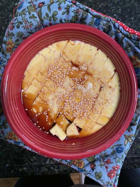 A glazed bake scored in diamonds and scattered with sesame seeds, in a red dish on a floral cloth