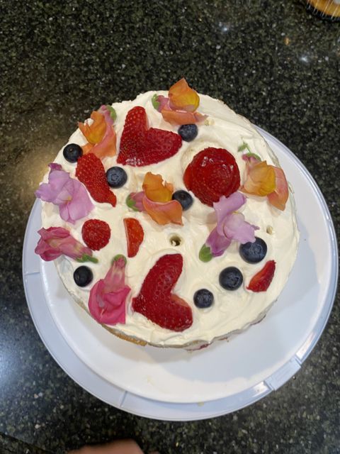 A cream-topped cake with strawberries, blueberries, and flower petals, from above