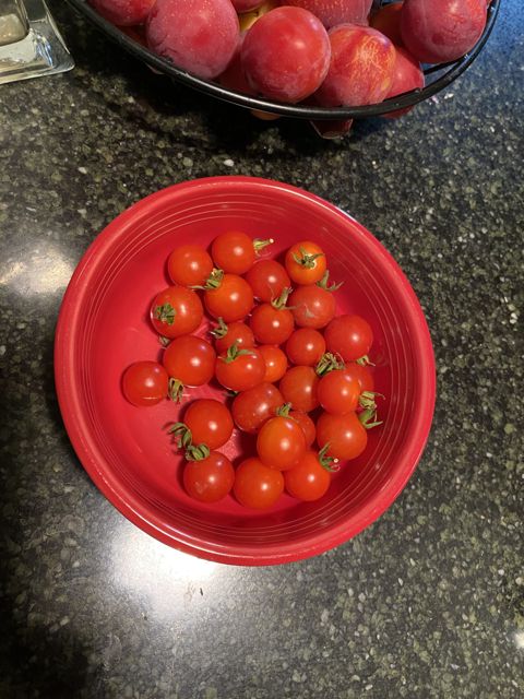 A red bowl of cherry tomatoes on the counter, peaches behind