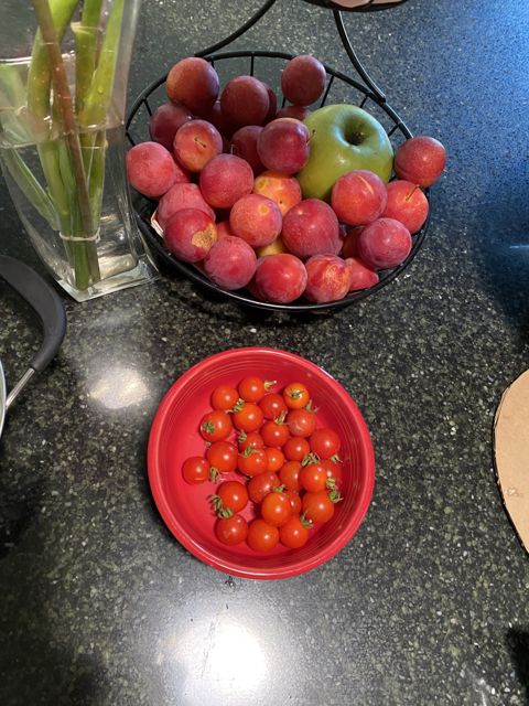 Cherry tomatoes in a red bowl beside a basket of peaches