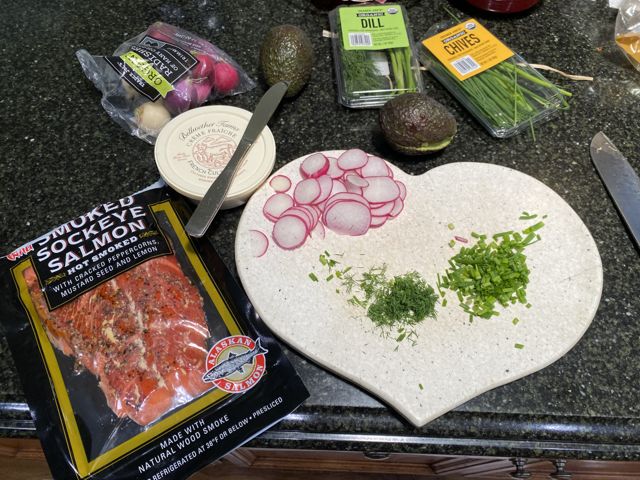 Smoked salmon, sliced radishes, and chopped herbs on a heart-shaped board