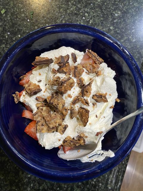 A blue bowl of whipped cream, strawberries, and crumbled topping