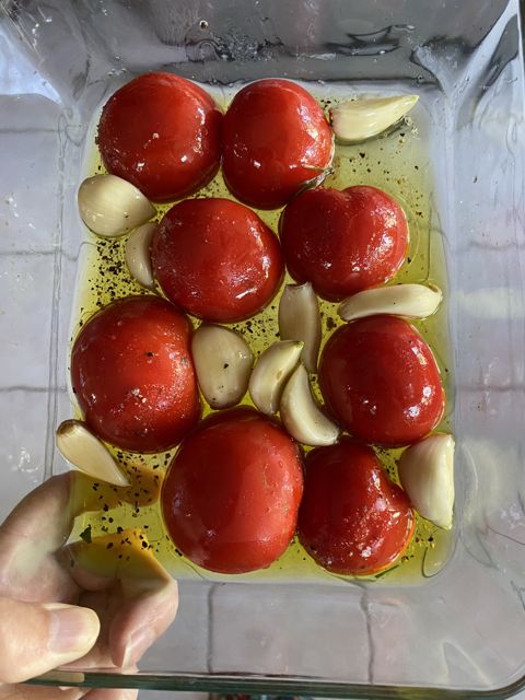 Tomatoes and garlic cloves in oil in a glass baking dish, ready for the oven