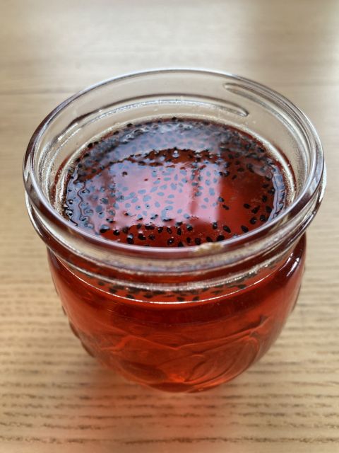 A glass jar of deep red drink flecked with seeds